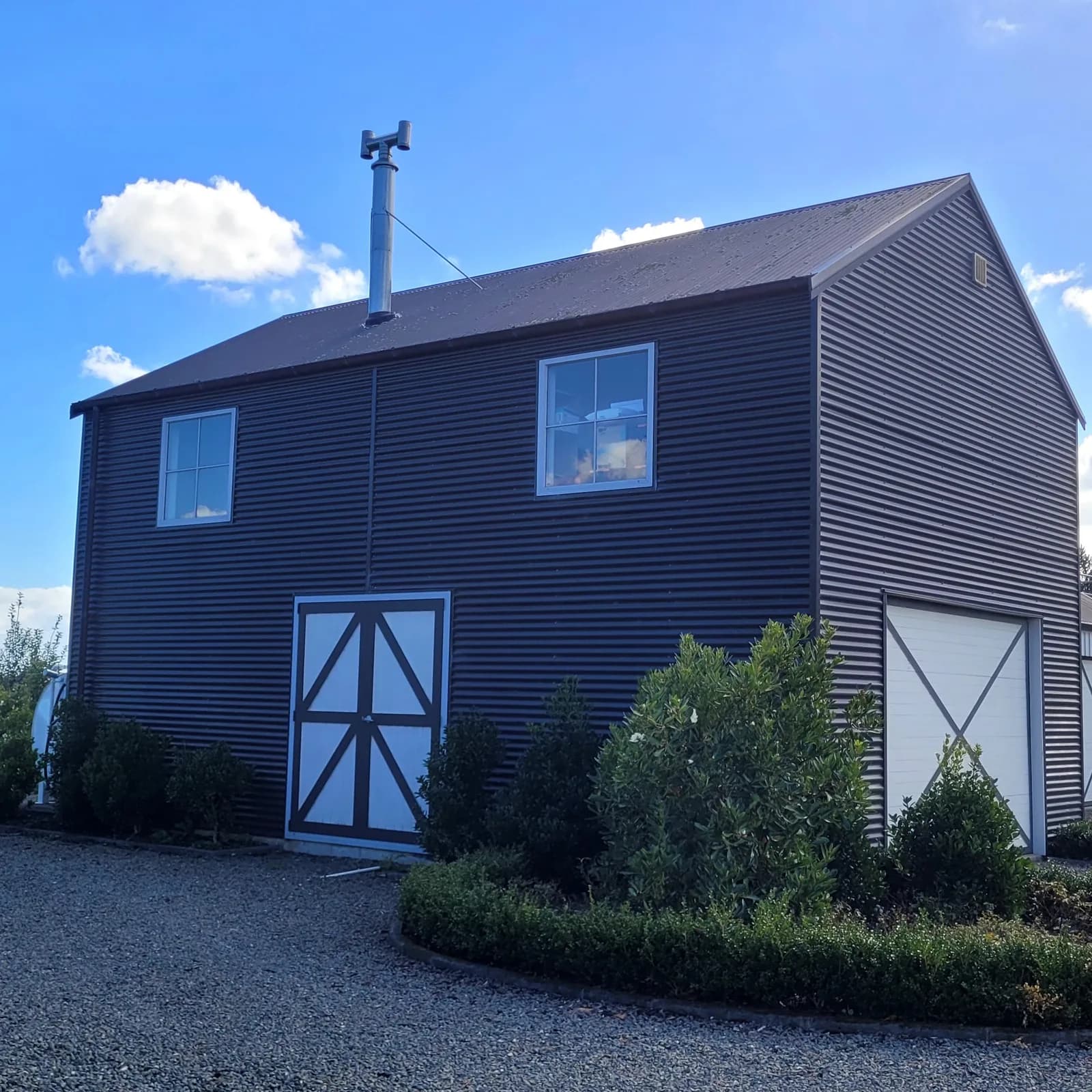Two-storey barn-style garage clad in dark corrugated iron with white cross-braced doors