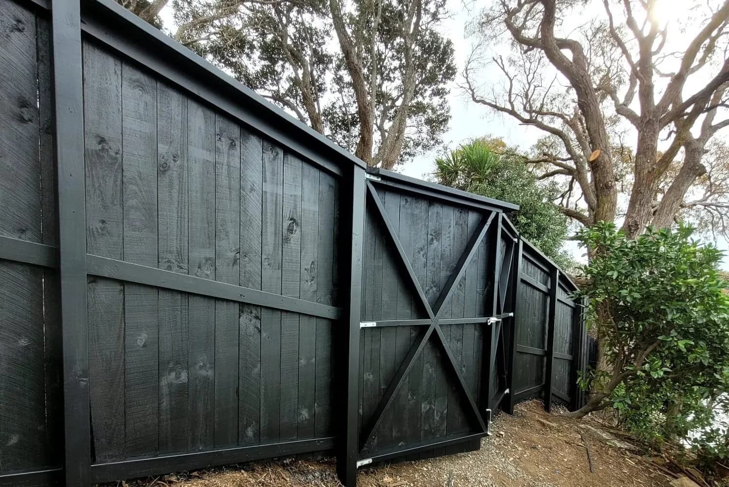 Timber boundary fence and gate stained black beneath mature trees