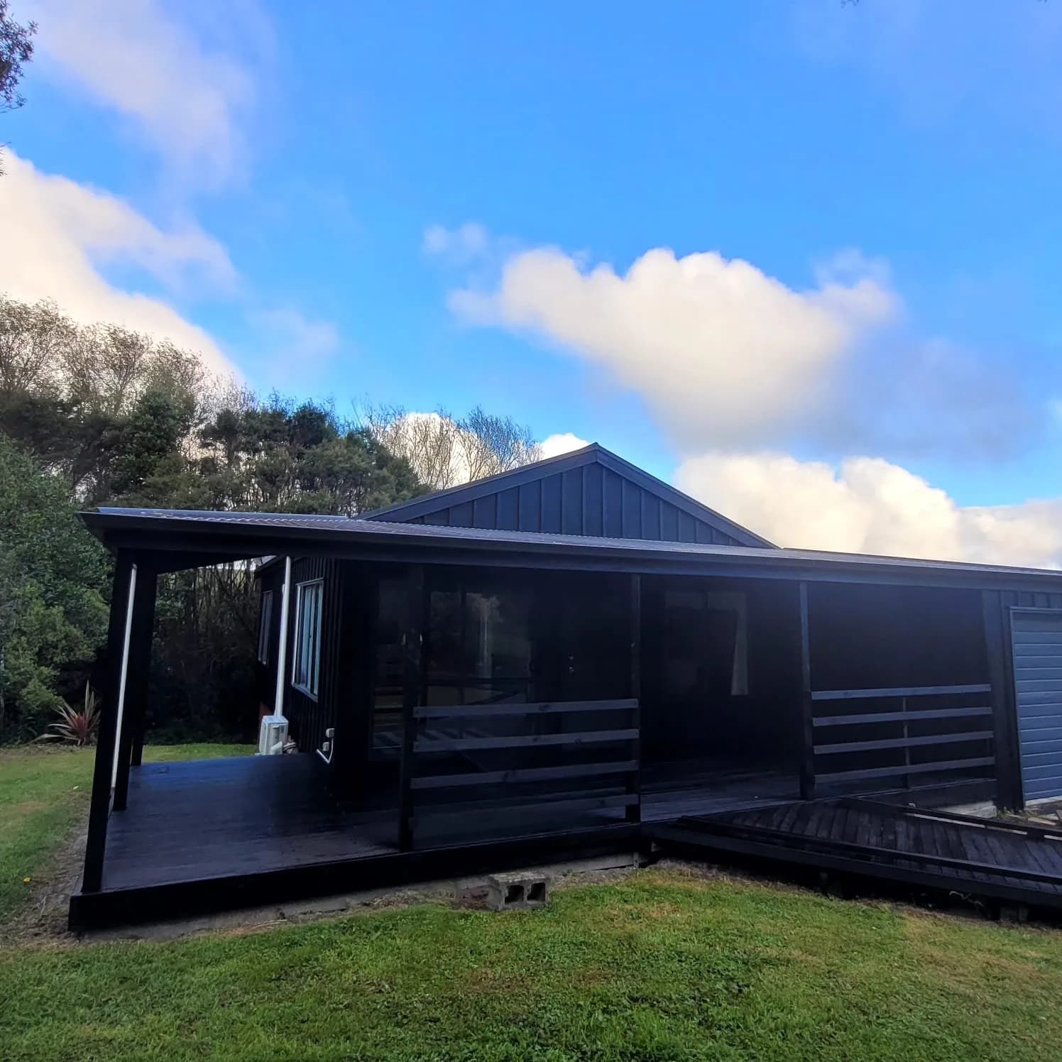 Black-stained house with a covered timber deck on a lawn