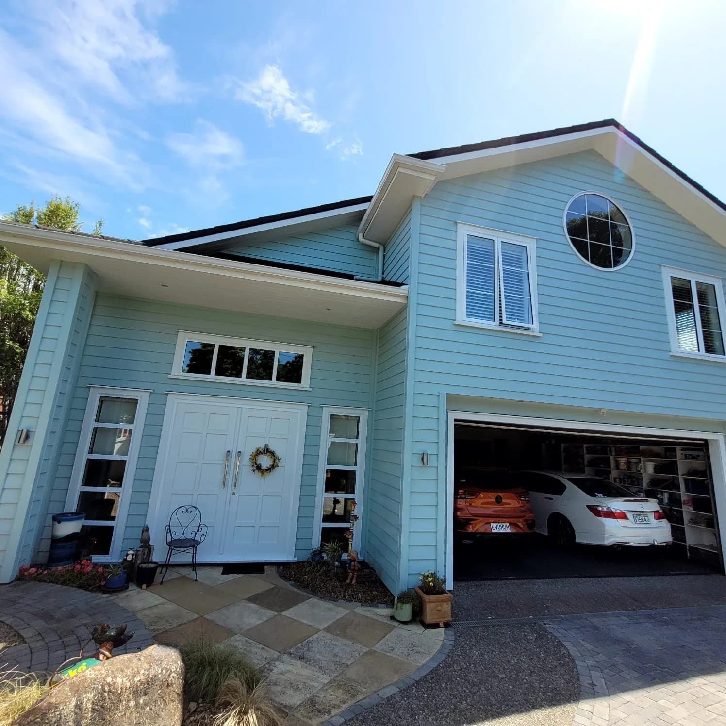 Light blue weatherboard house with white trim, round window and white front door after an exterior repaint