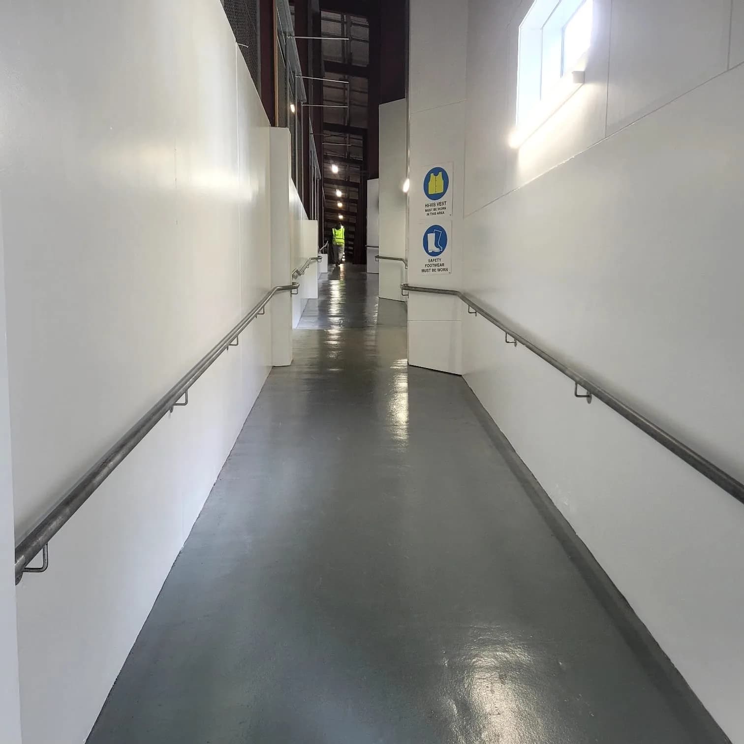 Long commercial corridor with white walls, grey floor and handrails