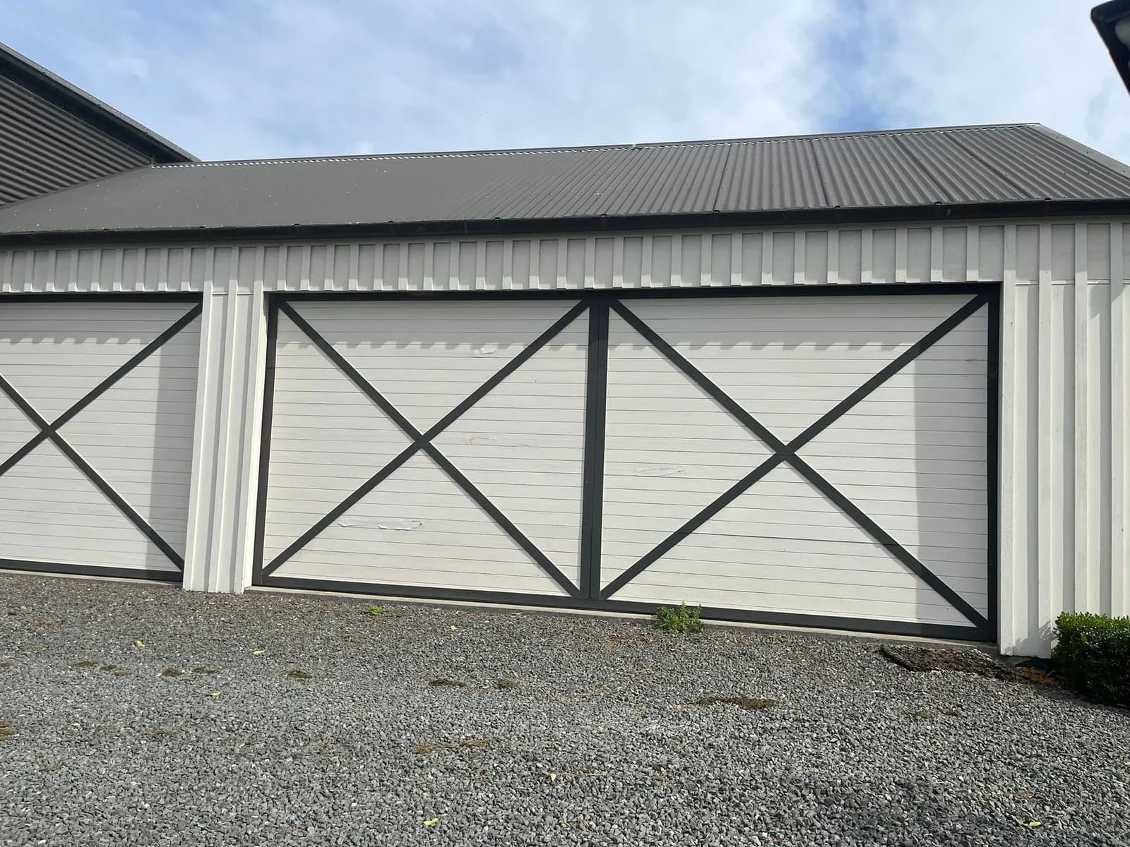 White garage doors with grey cross-brace trim on a gravel drive
