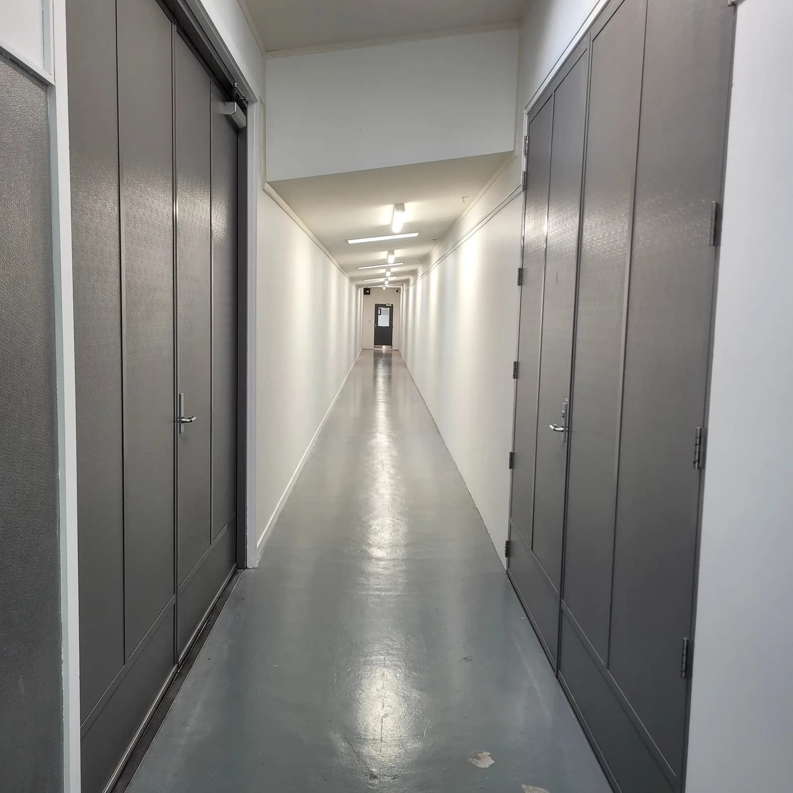 Long industrial corridor with white walls, dark grey doors and a grey painted floor