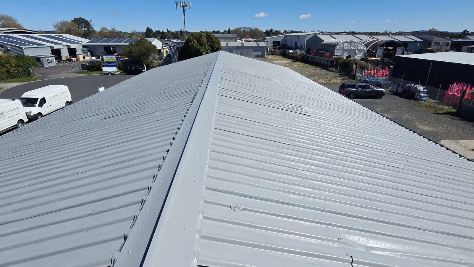 Long-run steel roof freshly painted light grey above an industrial area