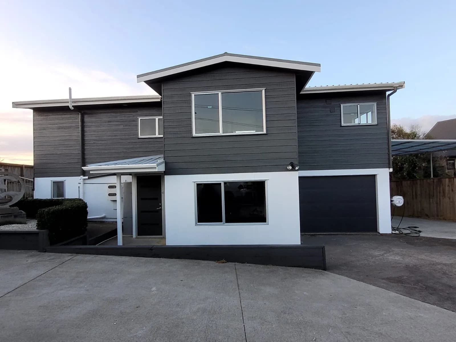 Two-storey house repainted in dark grey with a white lower level and white window trim, photographed at dusk