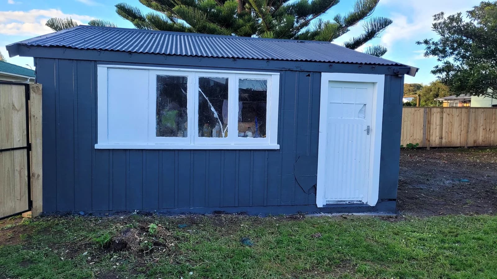 Small cabin repainted navy blue with a white door and white window joinery