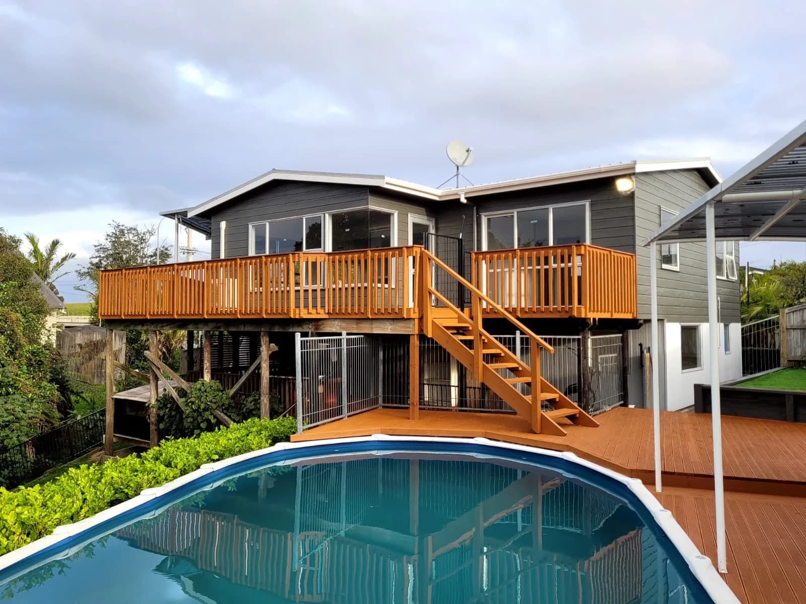 Dark grey house with a freshly stained timber deck and stairs beside a swimming pool
