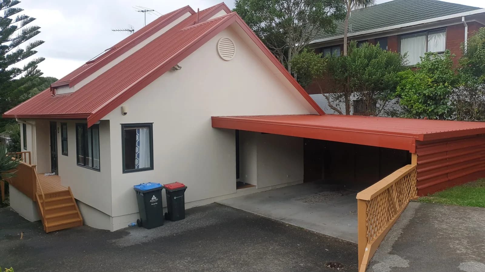 Cream house with a red roof, a matching red carport and stained timber steps and railings