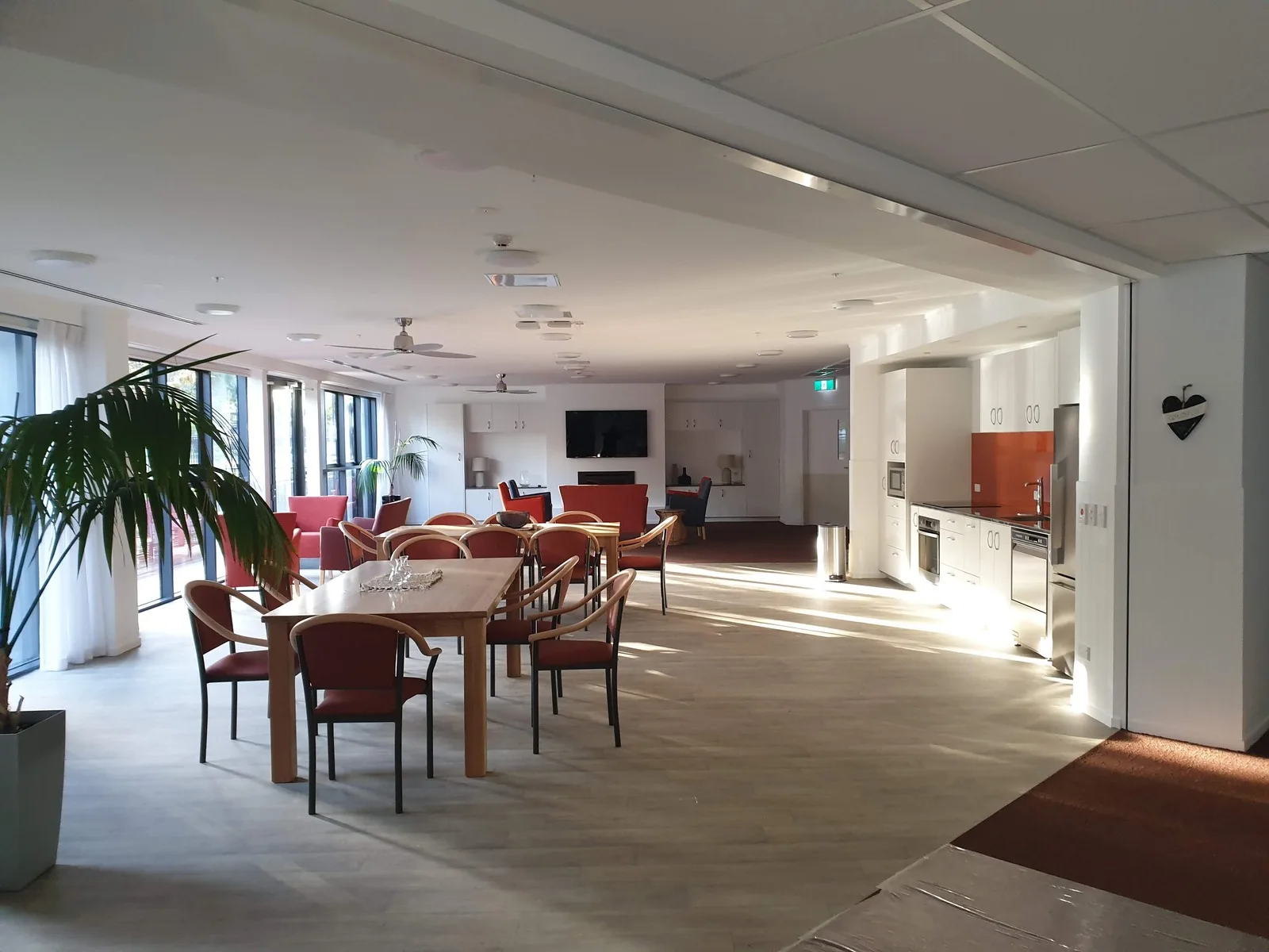 Large commercial staff room and kitchen with white walls and ceiling, dining tables and a pot plant