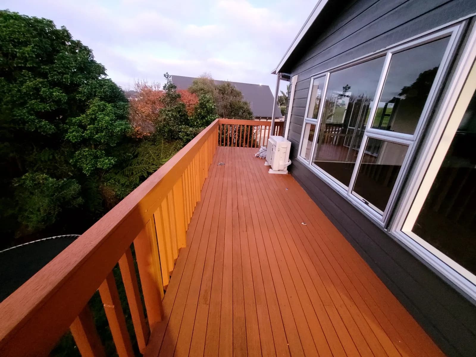 Upstairs timber deck and balustrade freshly stained orange alongside a dark grey house