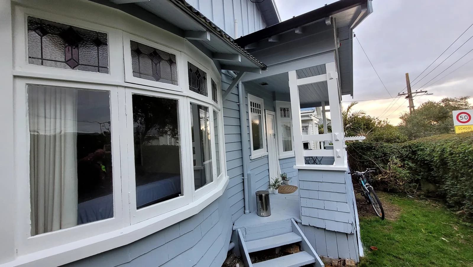 Pale blue villa with white-painted bay window joinery, leadlight top lights and a white entry porch