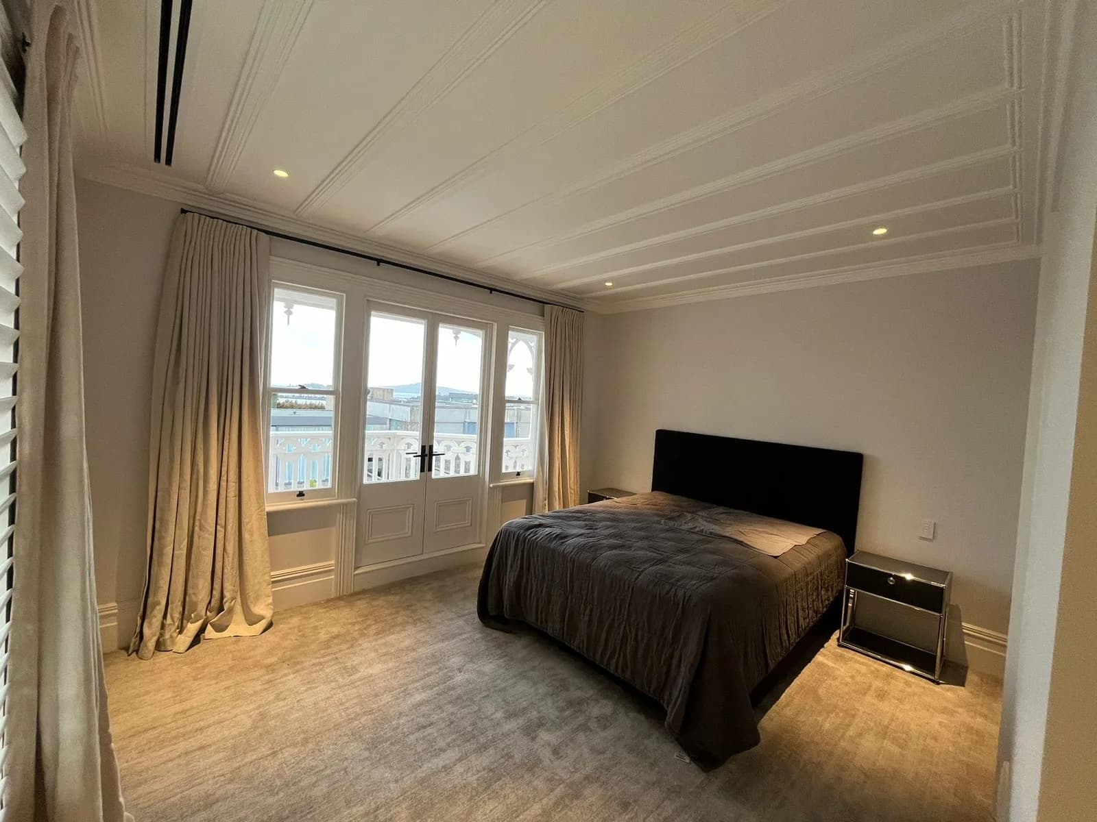 Bedroom with a white panelled ceiling, warm grey walls and French doors opening to a balcony