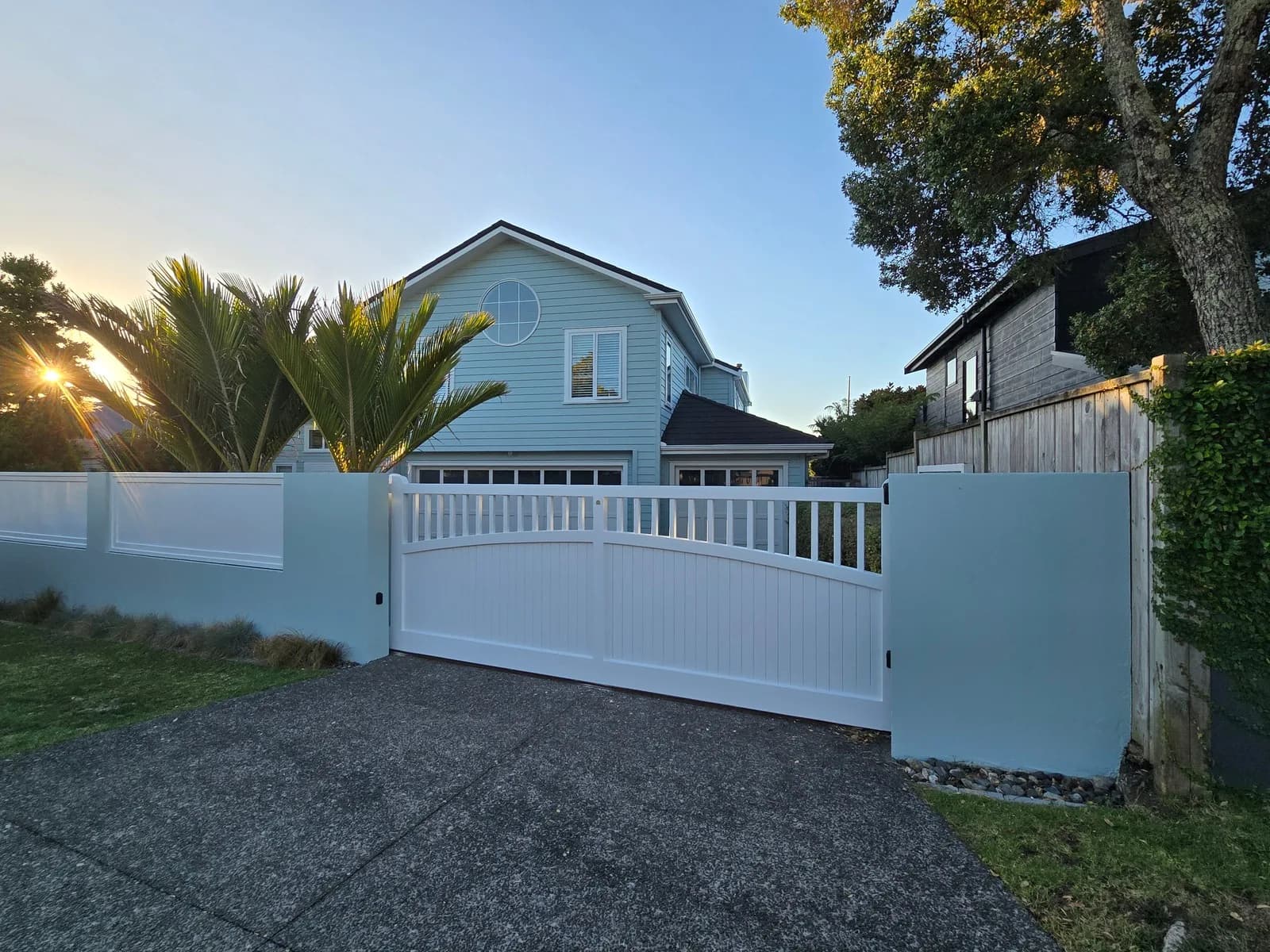 White sliding driveway gate and pale blue boundary walls in front of a blue two-storey house