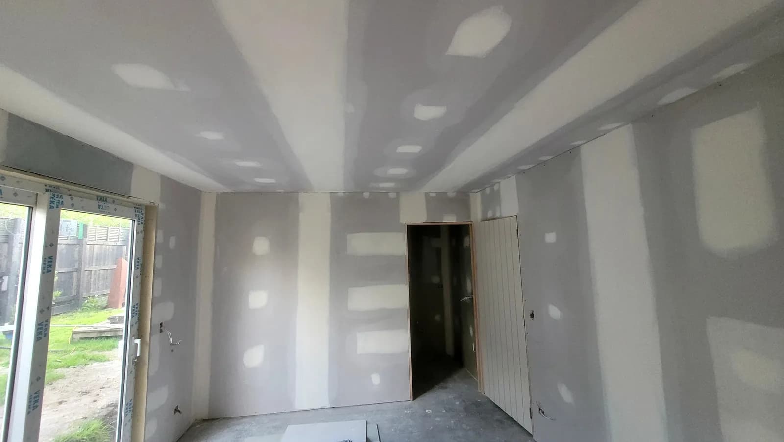 Living room with a sliding door, the plasterboard walls and ceiling stopped and ready for sanding